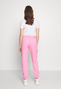 Różowe joggerki z elastycznymi mankietami i dopasowaną elastyczną talią, zestawione z prostą białą koszulką. Model odwrócony plecami do kamery.