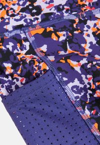 Tissu de sport violet avec un motif floral multicolore en orange, blanc et noir ; inclut une section inférieure texturée et perforée.