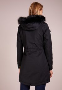 Schwarze Parka-Jacke mit Kapuze aus Kunstpelz, tailliertem Bund und Knopfdetails. Verfügt über einen geraden Schnitt und einen etwas längeren Saum im Rücken.