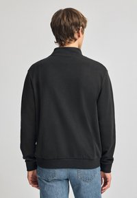 Zwarte rits sweatshirt met een zachte textuur, lange mouwen en een hoge kraag, gedragen met lichtblauwe jeans. Eenvoudig en casual ontwerp.