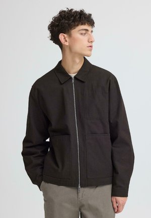 Dunkelbraune Jacke mit Kragen, Frontreißverschluss und zwei großen aufgesetzten Taschen. Der Stoff hat eine robuste Textur und eignet sich für legere Kleidung.