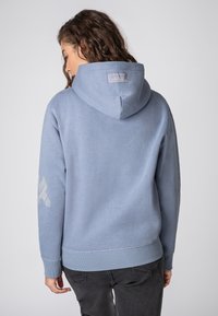 Lichtblauwe hoodie met een gestructureerde afwerking, voorzien van een logopatch op de achterkant en een grafisch ontwerp op de linker mouw, met ribgebreide manchetten en zoom.