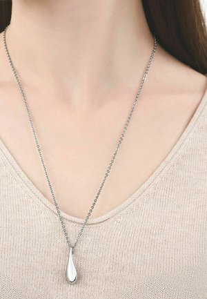 Collar de cadena de plata con un colgante liso en forma de lágrima, llevado por una persona que viste un suéter beige de punto.