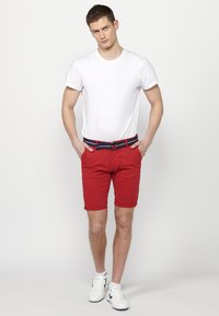 Shorts rouges avec des ourlets retroussés, dotés d'une ceinture bleu marine contrastante. Associés à un T-shirt blanc uni à manches courtes et des baskets blanches.