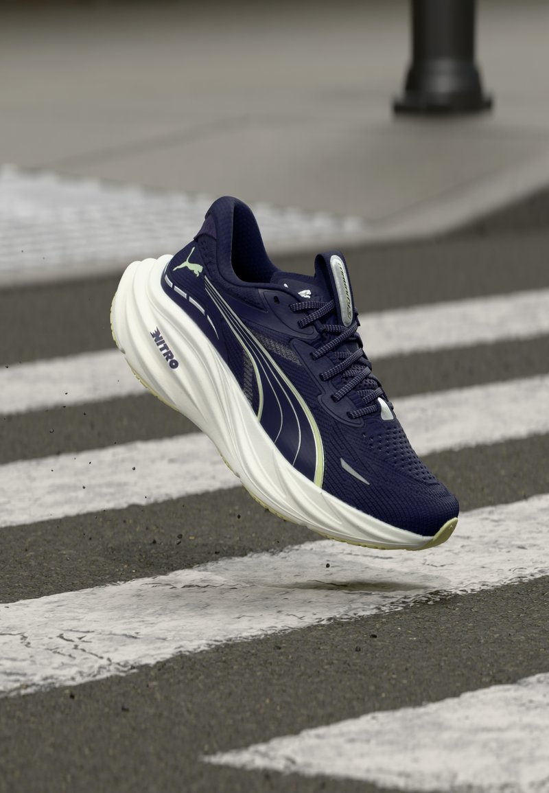 Ασπρόμαυρο αθλητικό παπούτσι Puma με παχιά σόλα που αιωρείται πάνω από διάβαση πεζών σε ασφαλτοστρωμένο δρόμο.