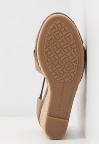 Sandale à talon compensé beige tissé, semelle en caoutchouc avec motif de T entrelacés et branding "Tommy Hilfiger" sur la semelle.