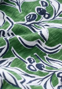 Grüner Stoff mit weißem und marineblauem Blumenmuster. Verfügt über eine weiche Textur und fließendes Design. Geschwungene Linien und kräftige Formen schaffen visuelles Interesse.