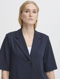 Tamno plavi blejzer s kratkim rukavima, s izrezanom larom i jednim gumbom za zatvaranje. Glatka, lagana tkanina s krojenim fitom.