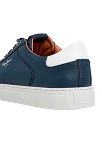 Zapatilla de cuero azul marino con acento blanco en el talón y suela de goma texturizada. Presenta puntera redonda, sistema de cordones y forro interior marrón.