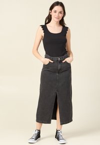 Svart ribbat linne med scallopade kanter, matchat med en högmidjad, lång svart denimkjol med en framklippning och fickor. Vita sneakers.