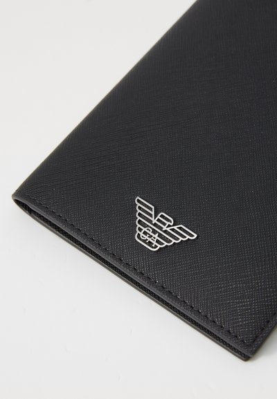 Čierna textúrovaná kožená peňaženka s pridaným strieborným logom s dizajnom krídla na prednej strane; obdĺžnikový tvar so zosilnenými okrajmi.