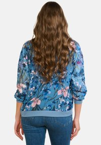 Zila ziedu bomber tipa jaka ar garām piedurknēm, uz kuras redzama rozā un zilu ziedu kombinācija, elastīgas aproces un ribota apakšmala.