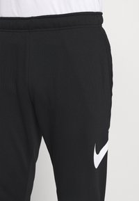 Pantalons de sport noirs en matériau doux avec une taille élastique et un logo Nike blanc bien visible sur le côté gauche.