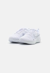 Une paire de baskets de course blanches Nike avec des lacets et des logos swoosh gris, placées côte à côte sur un fond blanc uni.
