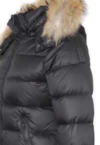 Giacca invernale nera trapuntata con cappuccio bordato in pelliccia, zip frontale e tasca laterale con zip, mostrata dalla spalla alla vita.