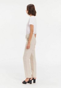 Pantalons beiges taille haute avec une jambe droite, associés à un t-shirt blanc à manches courtes et des sandales à plateforme noires.