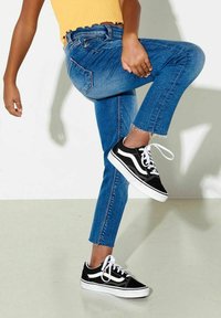 Jeans de denim azul de talle alto con dobladillo deshilachado, combinados con zapatillas Vans en blanco y negro con diseño clásico y cierre de cordones.