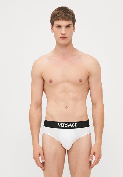 Fehér alsónadrág fekete derékrésszel, amelyen a "VERSACE" logó található. Egyszerű dizájn, sima textúra, testhezálló fazon és minimalista stílus.