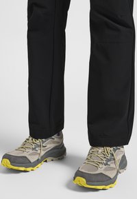 Leichte Wanderschuhe mit einem grauen und beigen Mesh-Obermaterial, gelben Akzenten und einer robusten Außensohle für Grip. Passen gut zu schwarzen Hosen.