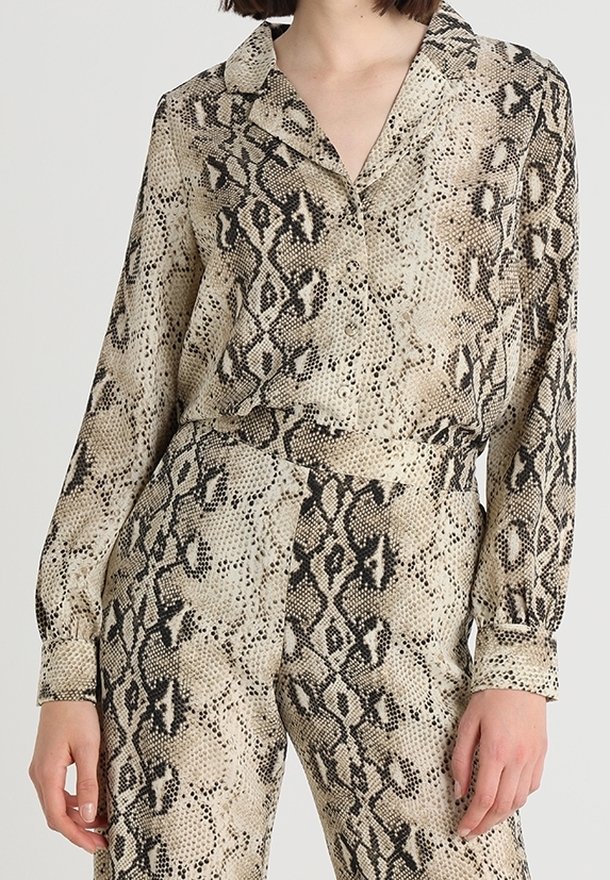 Komplet w wzór skóry węża w kolorze beżowym i czarnym, składający się z koszuli z kołnierzykiem oraz zwężanych spodni, wykonany z gładkiej, lekkiej tkaniny.