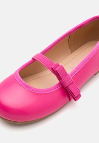 Kirev roosa balletti kingad ümmarguse varbaga, elastse rihmaga ja dekoratiivse paeltega. Sile nahakujuline materjal koos tekstuuriga sisekattega.
