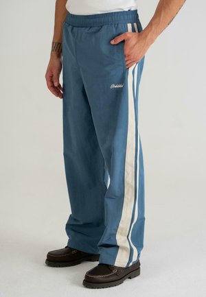 Pantalones de chándal azul claro con rayas blancas en los lados, cinturilla elástica y bolsillos laterales. Presenta un logo bordado en la parte frontal.