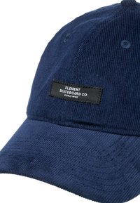 Marinblå kordfløyelskepp med en buet skygge, som har en svart etikett brodert på forsiden med "ELEMENT SKATEBOARD CO. WORLD WIDE."
