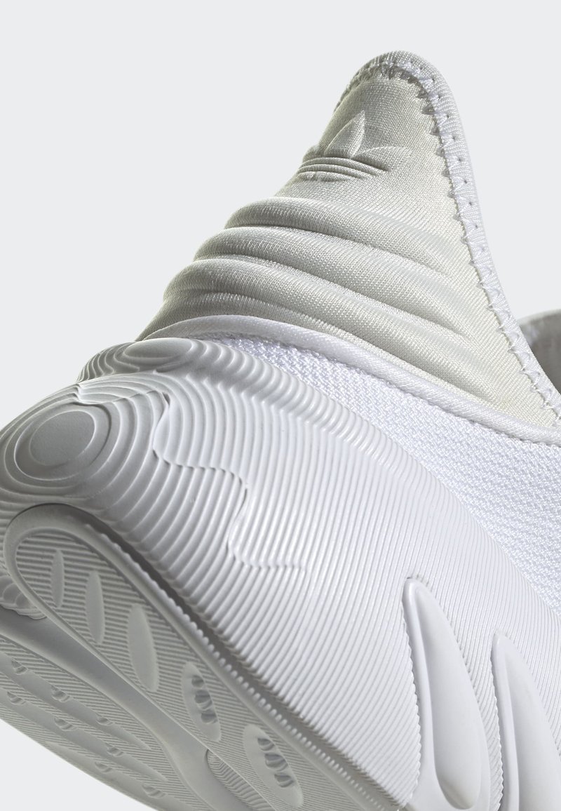 Białe sportowe buty z elegancką górą z materiału z teksturowanymi akcentami, zaokrąglonym obcasem i wzorzystą gumową podeszwą zapewniającą przyczepność.