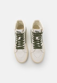 Höga sneakers med en krämfärgad mocka ovandel, gröna detaljer och matchande snören. Rundad tå och strukturerad sula utan synlig branding.