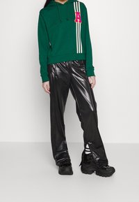 Felpa verde con la lettera "A" rosa e tre strisce bianche; abbinata a pantaloni neri lucidi e scarpe nere chunky.