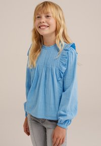 Modra, lahka bluza z dolgimi rokavi z nabranimi ramenskimi akcenti, pregibnim sprednjim dizajnom in nabranimi manšeti, v kombinaciji s svetlo sivo obleko.