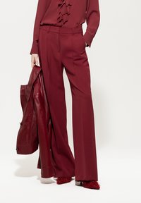 Burgunderfarbene, weit geschnittene Hosen mit Falten, kombiniert mit einer blusigen Bluse in passender Farbe und einer Lederjacke, alles in harmonierenden Farbtönen.