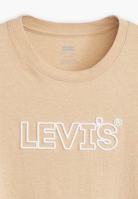 Beige puuvillane t-särk ümarate kraega ja valge tikkitud "LEVI'S" logoga. Sile tekstuur ja standardne lõige ilma täiendavate kaunistusteta.