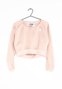 Sweatshirt court rose clair avec une surface texturée, manches longues, poignets côtelés, et un logo brodé sur la poitrine. Suspendu à un crochet noir.