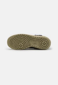 Semelle de chaussure Nike en caoutchouc beige, présentant un design texturé avec des motifs circulaires et des crêtes pour l'adhérence. Comprend un détail de logo.