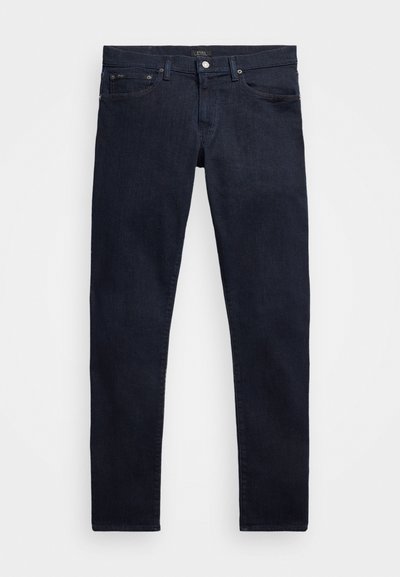 Jeans ajustados de color azul oscuro con cierre de botón y cremallera, trabillas para cinturón, bolsillos delanteros y traseros, extendidos sobre un fondo blanco.