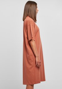 Preveliki T-shirt haljina od pamuka u boji hrđe. Kratki rukavi s savijenim manžetama, dužina do koljena i slobodan kroj. Glatka tekstura.