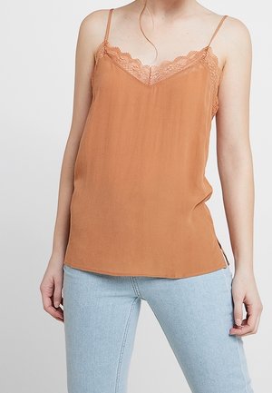 Ruskon väriinen cami-toppi, jossa on pitsireunus, säädettävät olkaimet ja pehmeä, sileä pinta. Yhdistetty vaaleansinihin kevyisiin farkkuihin.