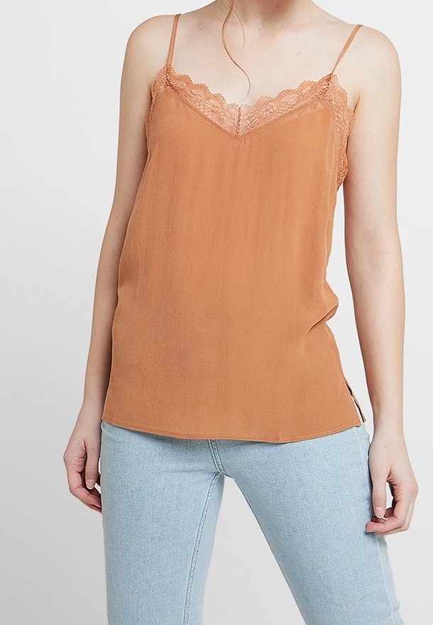 Rustrød cami-top med blondekant, justerbare spaghetti-stropper og en blød, glat tekstur. Bæres med lyseblå tætsiddende jeans.