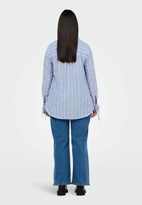 Blue and white striped long-sleeve shirt with tied cuffs, paired with blue flared jeans and black shoes. Viewed from the back.