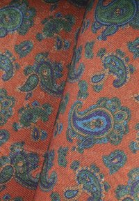 Tkanina z vibrantnym wzorem paisley w zieleni, niebieskim i fioletowym na terakotowym tle; widoczne detale tekstury materiału.