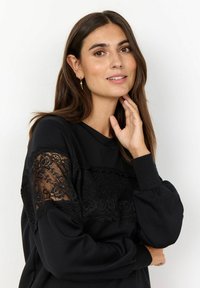Schwarzer Pullover mit einer Spitzenborte über der Brust, Ballonärmeln und einem runden Halsausschnitt. Weicher Stoff, lässiges Design.