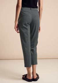Pantaloni alla caviglia a quadri verdi e bianchi con una vestibilità sartoriale, due tasche posteriori e una superficie liscia. Indossati con scarpe nere con punta aperta.