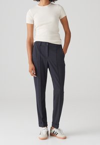 Mörkgrå skräddarsydda byxor med en subtil textur, med raka ben, uppvikta fållar och knappstängning, i kombination med en ljus krämfärgad figurnära t-shirt.