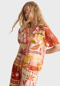 Camisa de manga corta con un estampado tropical en naranja, rosa y amarillo. Elaborada con una tela ligera, con un cierre de botones en la parte delantera y un corte relajado.