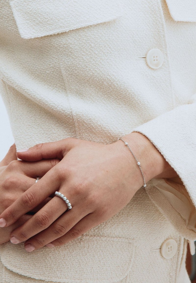 Zilveren ring met ronde stenen en een delicate zilveren armband met kleine kralen op een gemêleerde lichtbeige stof achtergrond.