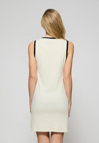Knielanges ärmelloses Kleid in Creme, mit geripptem Textur, schwarzer, einfarbiger Besatz am Rundhalsausschnitt und den Armöffnungen, figurbetonte Passform.