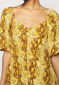 Gul och brun ormtryck klänning med fyrkantig halsringning och puffärmar; lättviktsmaterial med en strukturerad yta.