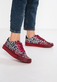 Des baskets à imprimé léopard présentent des accents noirs, roses et rouges avec une surface texturée, des lacets rouges et une semelle en caoutchouc. Convient pour une tenue décontractée.