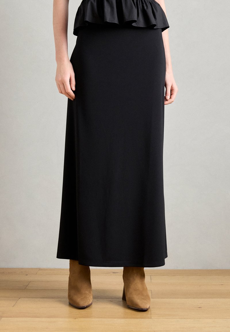 Jupe noire, longueur genoux, en tissu lisse ; design ajusté avec un ourlet évasé ; associée à des bottines en daim tan à la cheville.